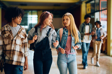 Female high school students talk while walking through hallway.