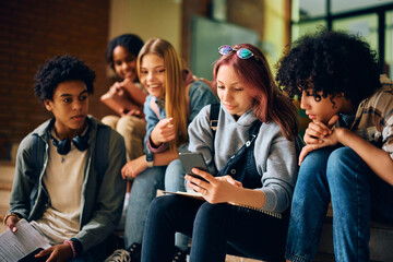 Teenage girl and her friends using mobile phone in hallway at high school.
