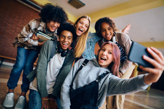 Multiracial group of cheerful teenage friends taking selfie at high school.