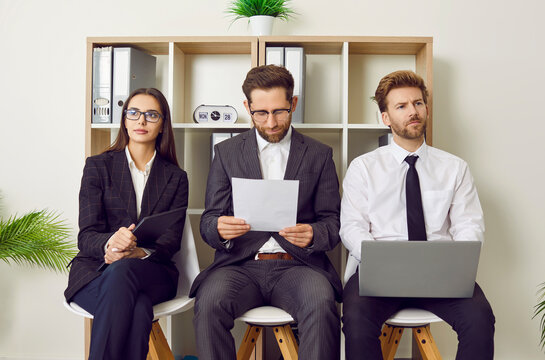 Young business people sitting on the chairs in a row with resumes and laptops in hands. Group of a staff and company employees at work. Job candidates seekers waiting for interview invitation turn.