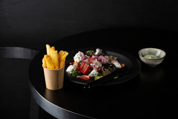 Greek salad and french fries on black table