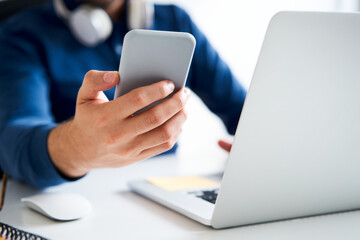 Closeup of man holding smartphone next to laptop screen sitting at a desk