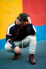 Young caucasian man posing for a sunglasses advertisement. Colorful painted wall. Graffiti wall.