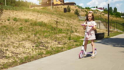 Child riding scooter. little girl rides a pink scooter on the road in a park outdoors on a summer day, active children playing outdoors, a healthy lifestyle concept for children