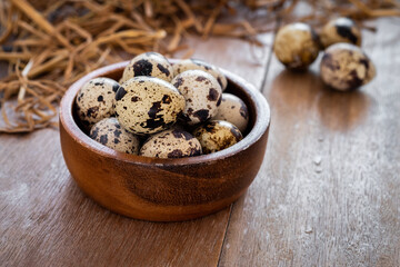 Quail eggs in wooden bowl and dry straw on old table