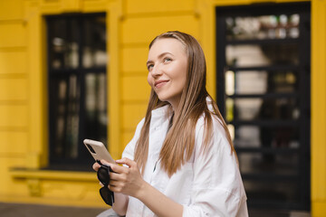 Dreamy and excited happy young blonde woman using mobile phone, smiling and looking thoughtful at side, have idea, search solutions, thinking. Blonde girl look dreaming and flirting, look at side.