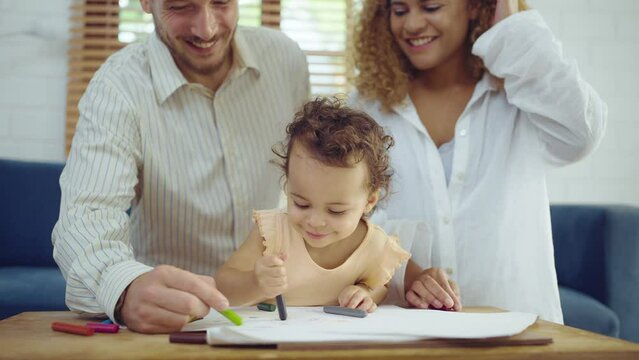 Dad, Mom and little daughter drawing with colorful pencils on paper happy smiling.Young family spend free time together in living room at home.