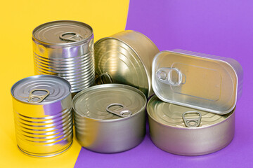 A Group of Stacked Tin Cans with Blank Edges on Split Yellow and Violet Background. Canned Food. Different Aluminum Cans for Safe and Long Term Storage of Food. Steel Sealed Food Storage Containers