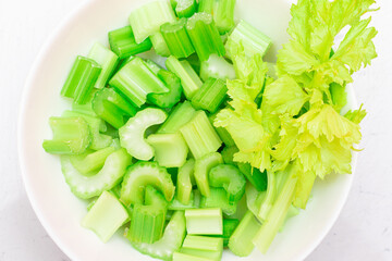 Fresh Chopped Celery Slices with Water Drops on White Dish - Top View. Vegan and Vegetarian Culture. Raw Food. Healthy Diet with Negative Calorie Content