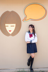 woman wearing a Japanese school uniform stands with a cute pattern in the background. Copy space