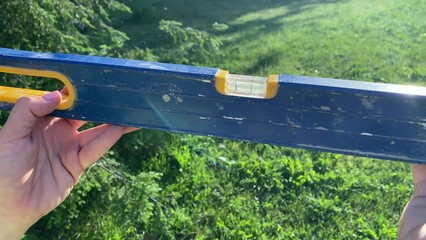 Adult woman holds spirit level balancing bubble tool in golden sun rays outdoors. Balance concept. Landscape garden at sunrise on background. Analogy to work life balance finding equilibrium