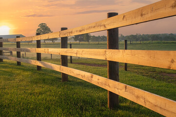 Sunrise lights an arching split rail fence on the farm - Powered by Adobe