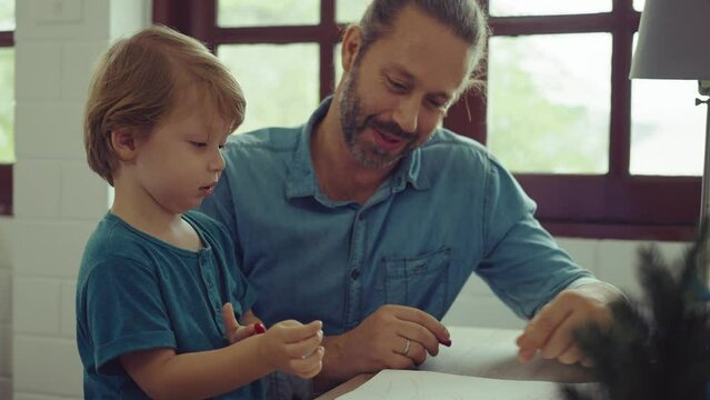 Caucasian family painting on paper with son indoors in house. Little son learn how to draw art picture enjoy creativity with father in house.