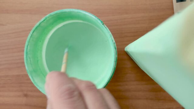 Man's Hand Stirring Green Turquoise Water Paint with a Wooden Stick. Getting Ready to Paint a Chair Leg.