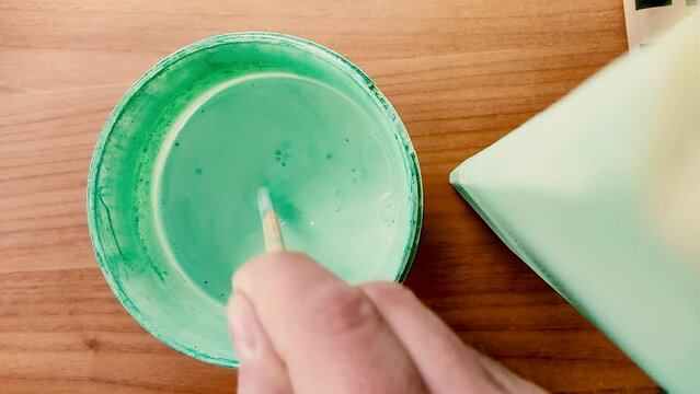 Man's Hand Stirring Green Turquoise Water Paint with a Stick. Getting Ready to Paint a Chair Leg. High Contrast