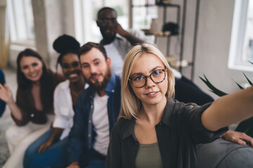 Happy excited diverse colleagues sitting in sofa taking selfie