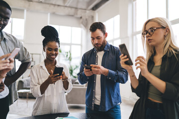 Diverse colleagues using smartphones in office standing together
