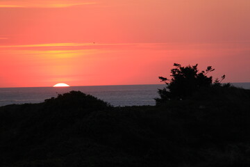 at the sea the red-golden sun shines out from behind the clouds before it sets