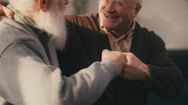 Smiling senior buddies bumping fists and talking at home, strong friendship