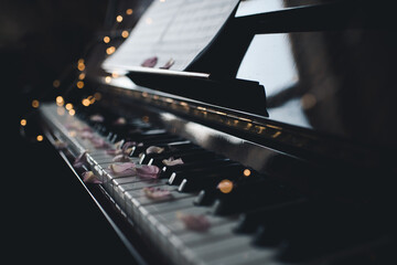 Vintage old grand piano with rose flower petals on keys with glowing lights closeup. Valentines Day. © morrowlight