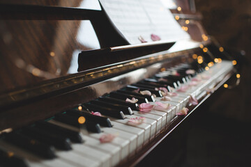 Vintage old grand piano with rose flower petals on keys with glowing lights closeup. Valentines Day.