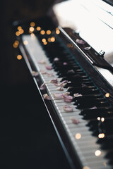 Vintage old grand piano with rose flower petals on keys with glowing lights closeup. Valentines Day. © morrowlight