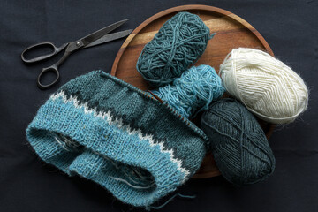 Turquoise green white wool knitted sweater on the metal needles with yarn balls and vintage scissors, stockinette stitch knitting in progress close-up photo