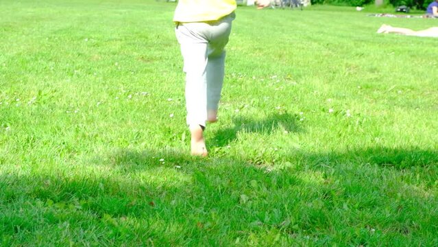 A Barefoot 7-year-old Girl In Gray Pants Runs Away Into The Distance On The Grass. Carefree Happy Childhood.