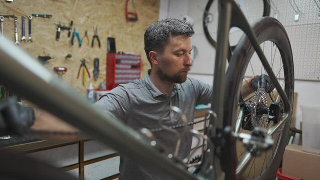 Man bicycle mechanic installs cycle chain on bike. Technician fixes bicycle chain gear at bicycle repair shop. Bicycle mechanic adjusts bike chain. Mechanical engineer fixing transmission in workshop