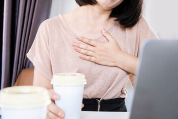 Asian woman having problems with heart palpitations or heart beating too fast after drinking coffee and too much caffeine - obrazy, fototapety, plakaty