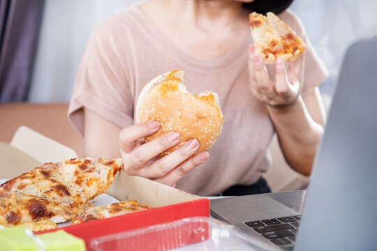 Binge Eating Disorder concept with woman over eating Fast Food Burgers and Pizza at an Office Desk