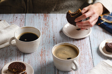 Girl drinking coffee and eating chocolate alfajores on a wooden table.