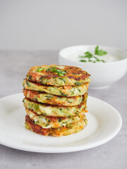 golden brown stacked vegetable and cheese pancakes or fritters, in the background unfocused bowl with yogurt and herb sauce