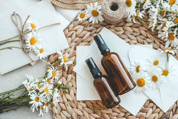 Composition with chamomile flowers and cosmetic bottle of essential oil on white background, top...