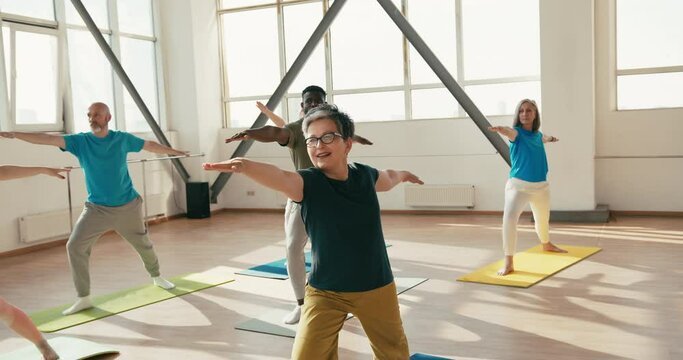 Group of senior athletes stretches upper body in sunny gym