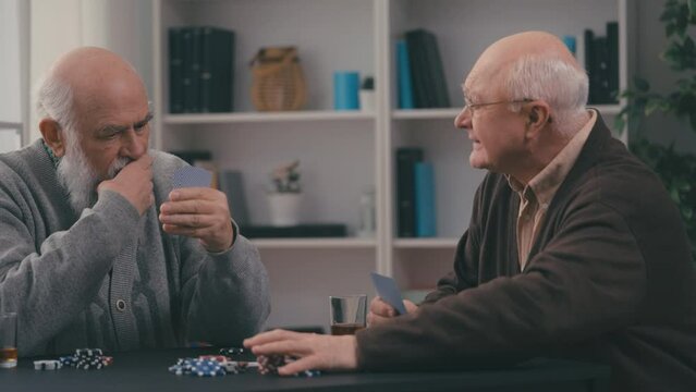 Two elderly male friends playing poker at retirement home, leisure time
