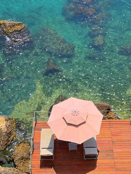 Beach sunbeds and sunshade on sea shore of rocky coast.