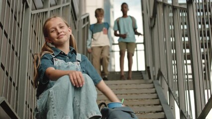 Low angle portrait of pretty Caucasian preteen schoolgirl smiling at camera sitting on stairs outdoors while her diverse classmates going down in slowmo - Powered by Adobe