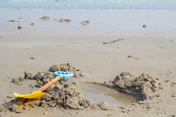 Plastic toy shovel on the sand. Children having fun digging sand while going to the sea on their summer vacation.