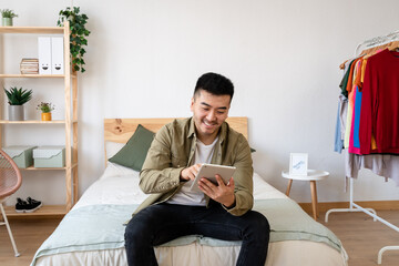 Young man sitting in bed using digital tablet.