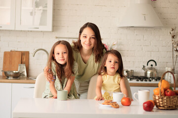 portrait of mother and daughters sitting at the table and holding drinks looking directly at the camera in the kitchen
