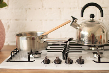 Stainless steel kettle standing on an unlit gas burner on the hob in a kitchen with tiled white...