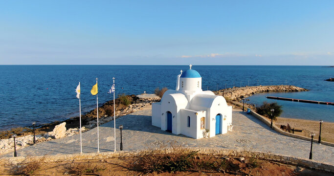 Drone shooting a small beautiful white church or Chapel of St. Nicholas with a blue dome and a door on the shore of a calm deep sea in Protaras Cyprus.