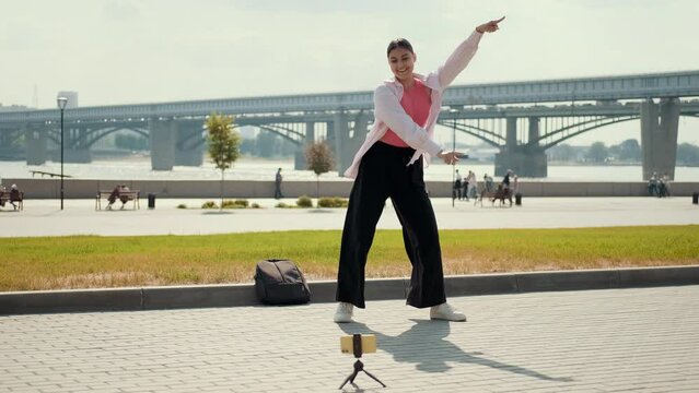 Energetic girl streaming media content using smartphone while dancing on the street