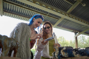 Two fashionable and diverse females buying pottery at flea market sale. Portrait of a cheerful LGBT...