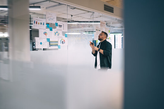 Male entrepreneur drawing on glass wall working with charts