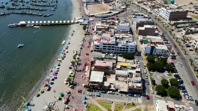 Aerial shot drone flies forward with camera angled down over Paracas with boat marina and beach to the left