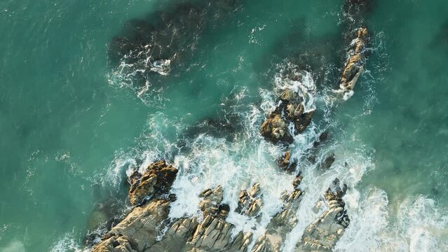 Zoom in top down aerial view waves splashing rocks