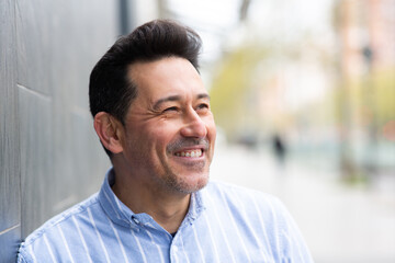 Obraz premium Cheerful mature latin man leaning to a wall outside