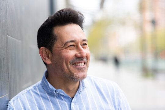 Cheerful mature latin man leaning to a wall outside